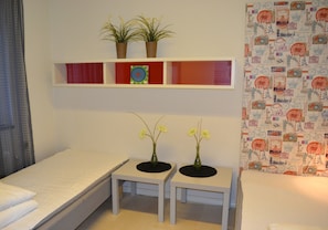 Een hotelkamer met een bed, twee kleine tafels met vazen, een plank met planten en een behang met patroon.