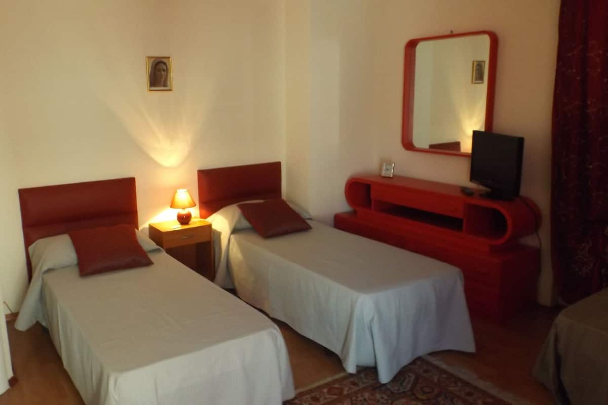 A room with two single beds, a nightstand with a lamp, a red dresser, and a mirror on the wall.