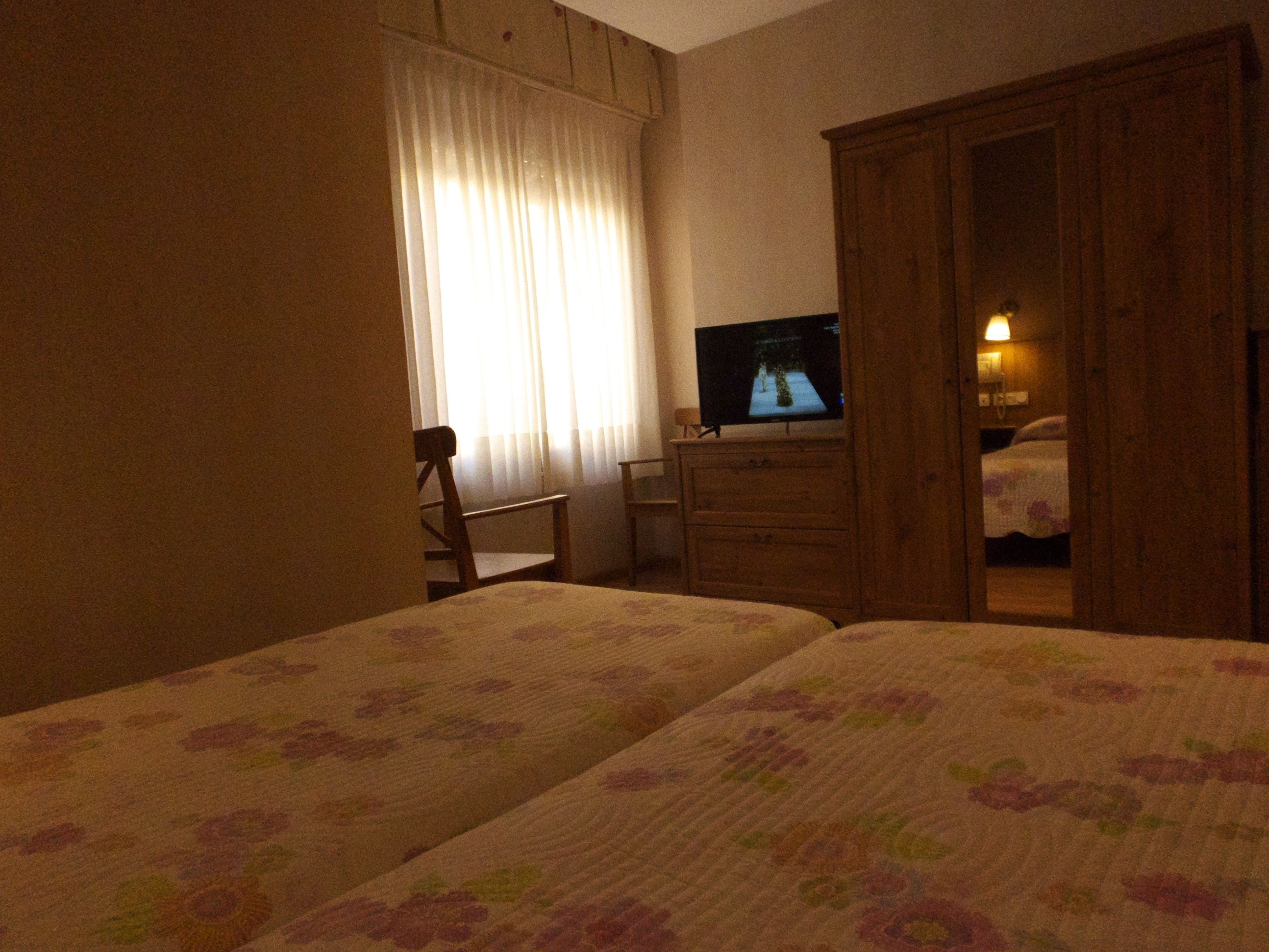 Habitación de hotel con dos camas, una televisión, un armario de madera y una silla.