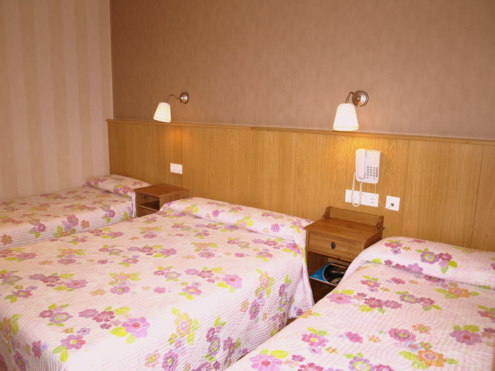 A hotel room with two single beds, wooden headboards, bedside tables, and a wall-mounted telephone.