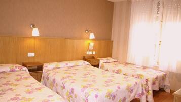 A hotel room with three single beds, wooden headboards, a wooden nightstand, a telephone, and a window with curtains.