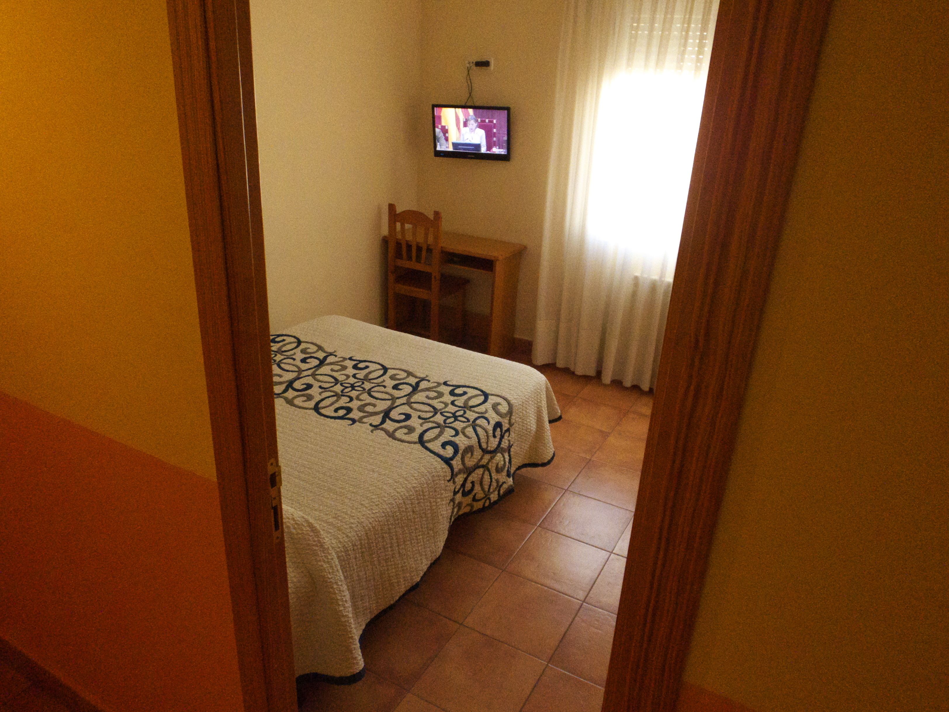 Una habitación de hotel con una cama, un televisor montado en la pared y una mesita.