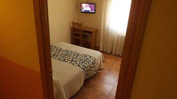 Una habitación de hotel con una cama, un televisor montado en la pared y una mesita.