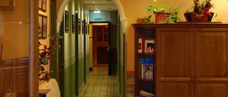A hallway with a wooden cabinet, a table with a white tablecloth, and a potted plant on a shelf.
