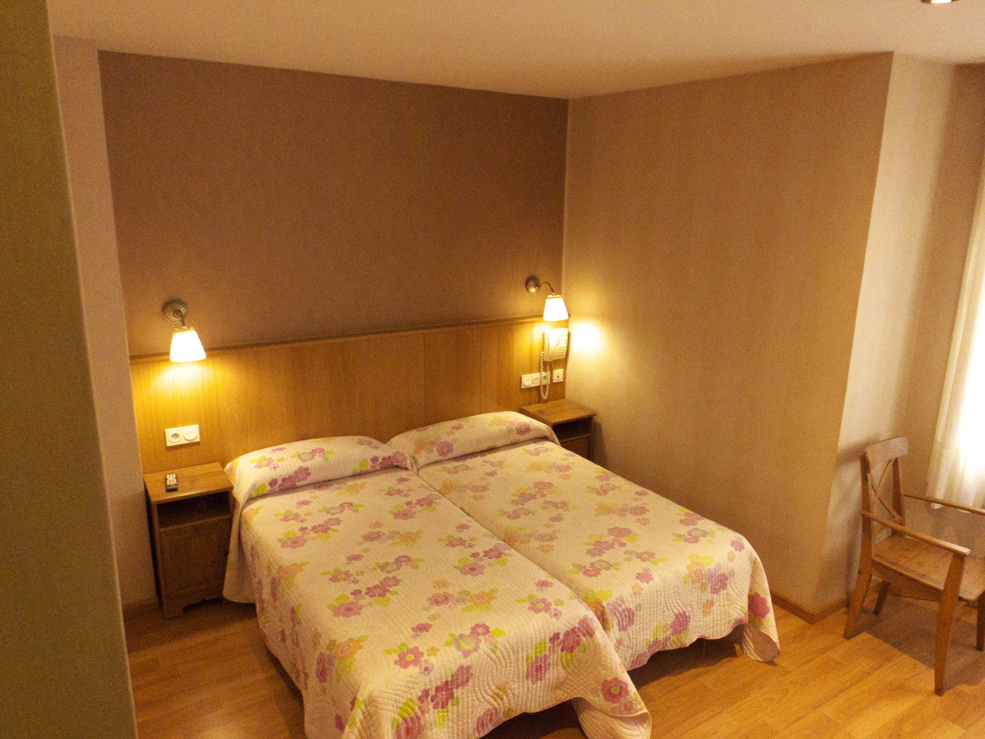 Una cama doble con ropa de cama floral, lámparas de noche, una mesita de noche de madera y una silla de madera.