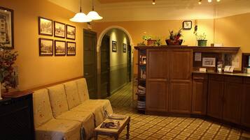 A cozy hotel lobby with a sofa, a wooden cabinet, and framed pictures on the wall.