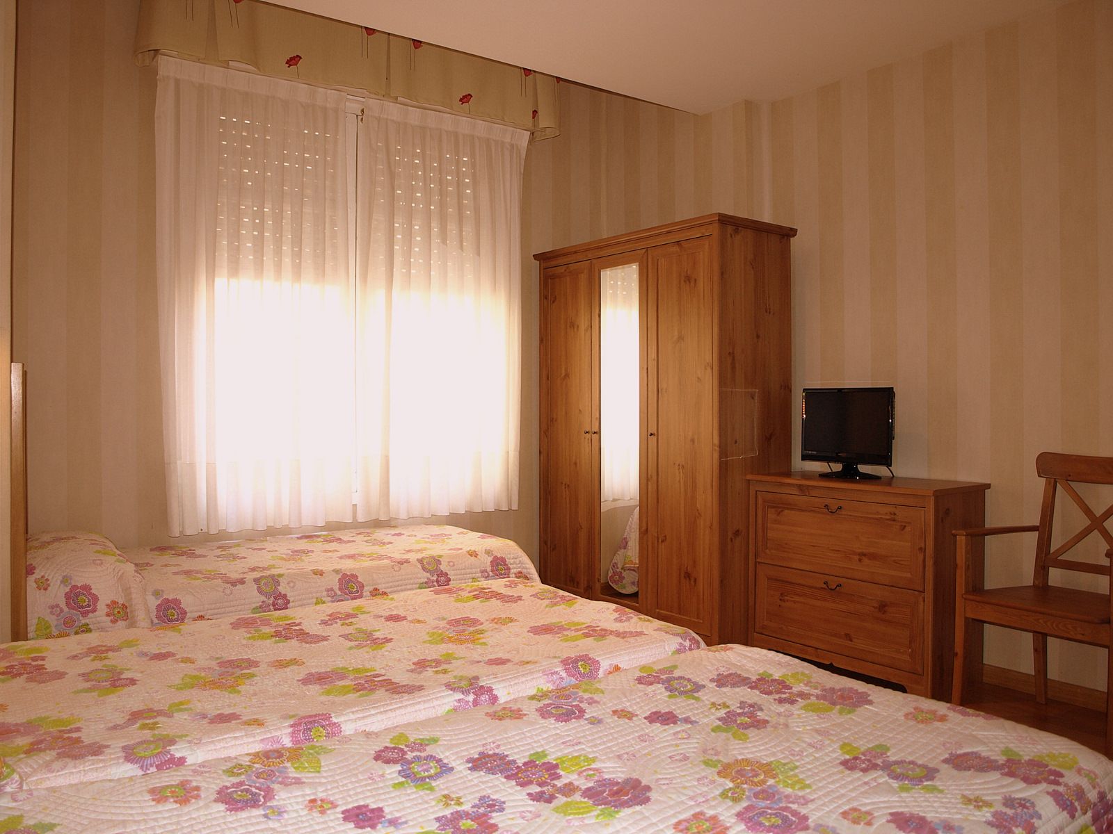 Ein Schlafzimmer mit zwei Betten, einem Holzschrank, einem Fernseher auf einer Kommode und einem Sessel.