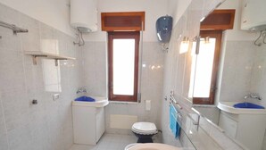 A compact bathroom with a bathtub, two sinks, a toilet, and a window. - Amami Viaggi - Casa Venere (Capaccio-Paestum)