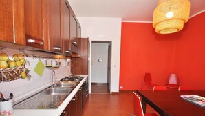 A kitchen with wooden cabinets, a stainless steel sink, and a red dining area with a table and chairs. - Amami Viaggi - Casa Venere (Capaccio-Paestum)