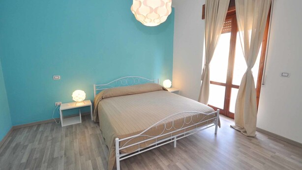 A bedroom with a bed, bedside tables, a hanging light fixture, and a window with curtains. - Amami Viaggi - Casa Venere (Capaccio-Paestum)