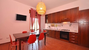 A modern kitchen with wooden cabinets, a dining table with red chairs, and a hanging light fixture. - Amami Viaggi - Casa Venere (Capaccio-Paestum)