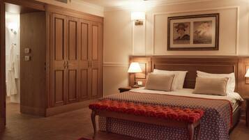 Una habitación de hotel con un armario de madera grande, una cama con dos almohadas, una mesita de noche con una lámpara y una alfombra roja estampada.