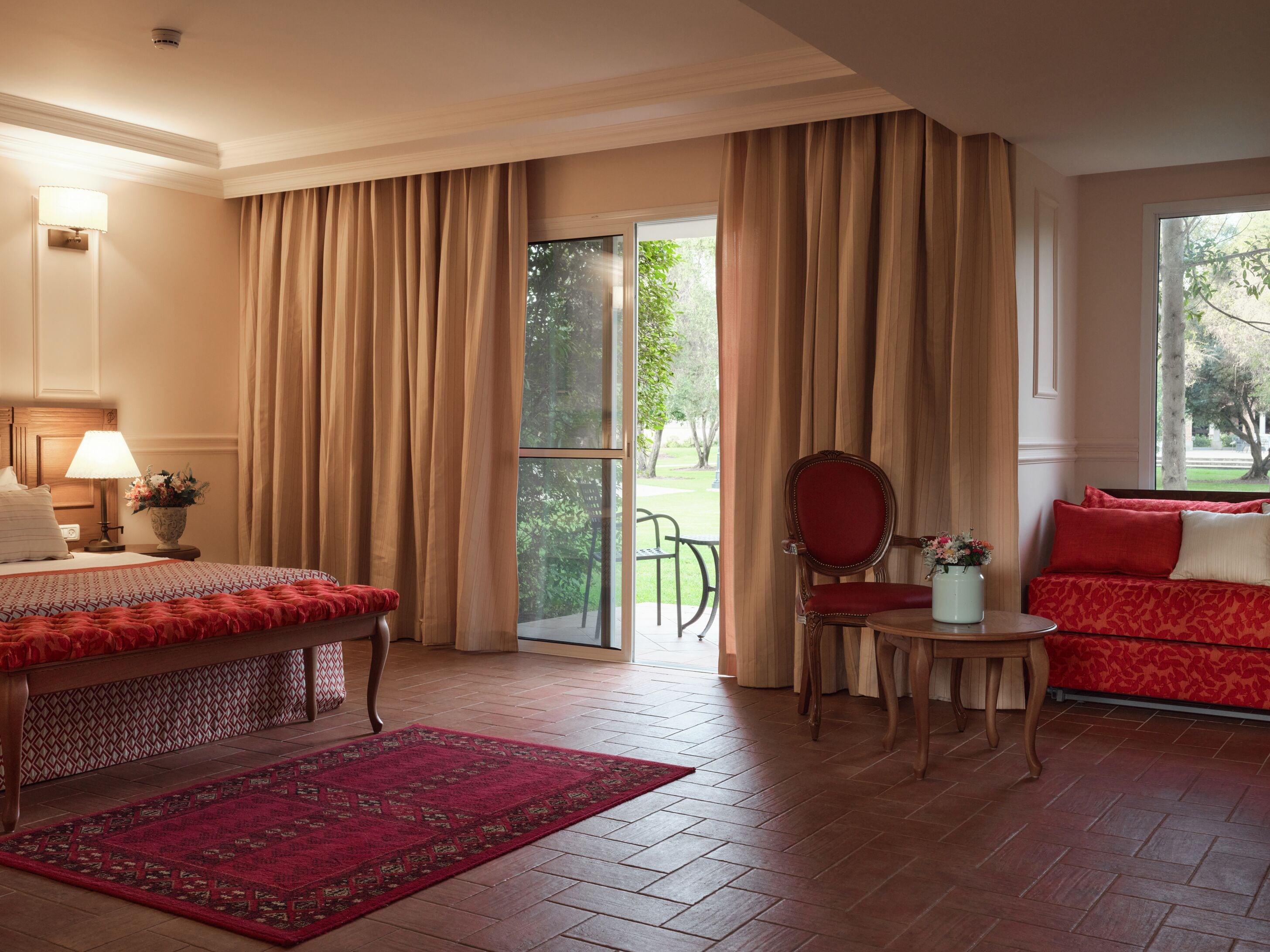 Une chambre d’hôtel avec un lit, une chaise, un canapé, une petite table et une fenêtre avec des rideaux.