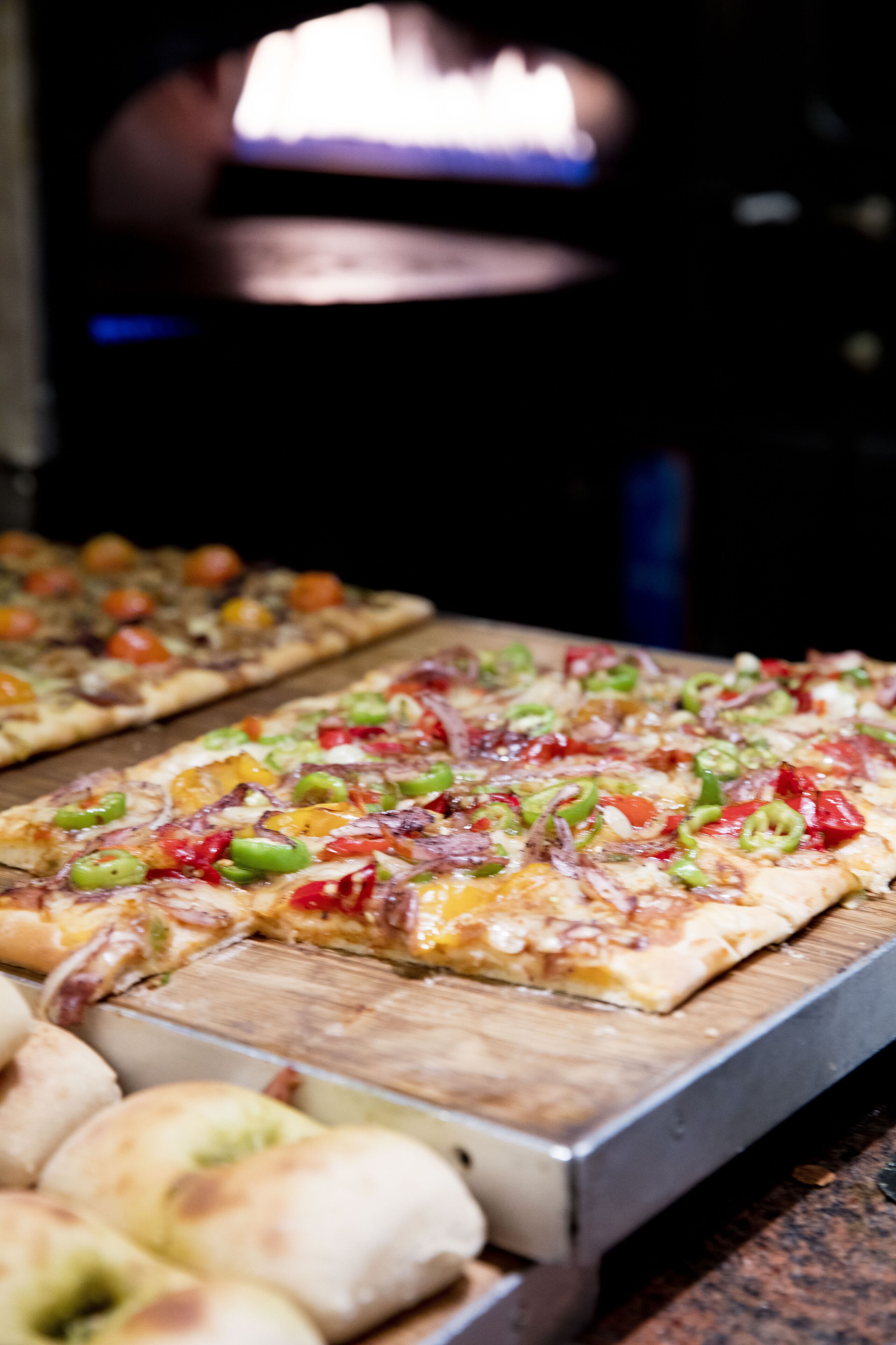 A pizza oven with pizzas and bread rolls on a wooden board.