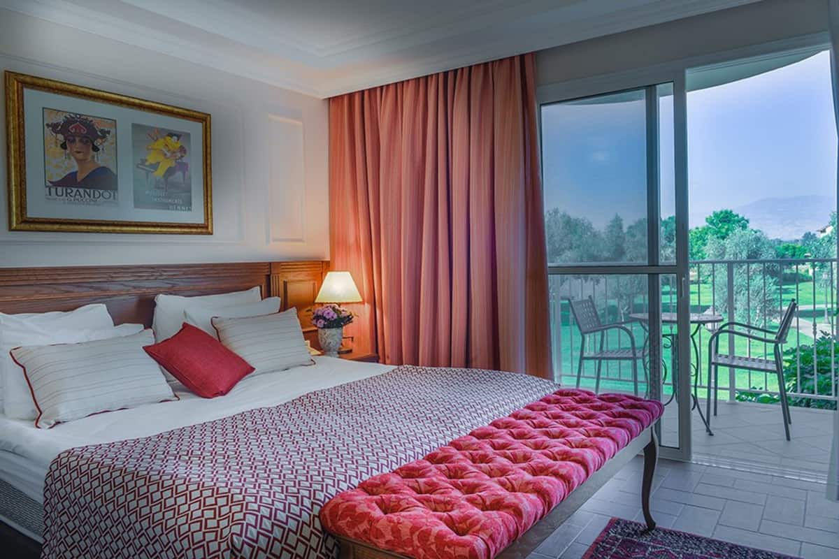 Une chambre d’hôtel avec un grand lit, un balcon avec des chaises et une vue sur l’extérieur.