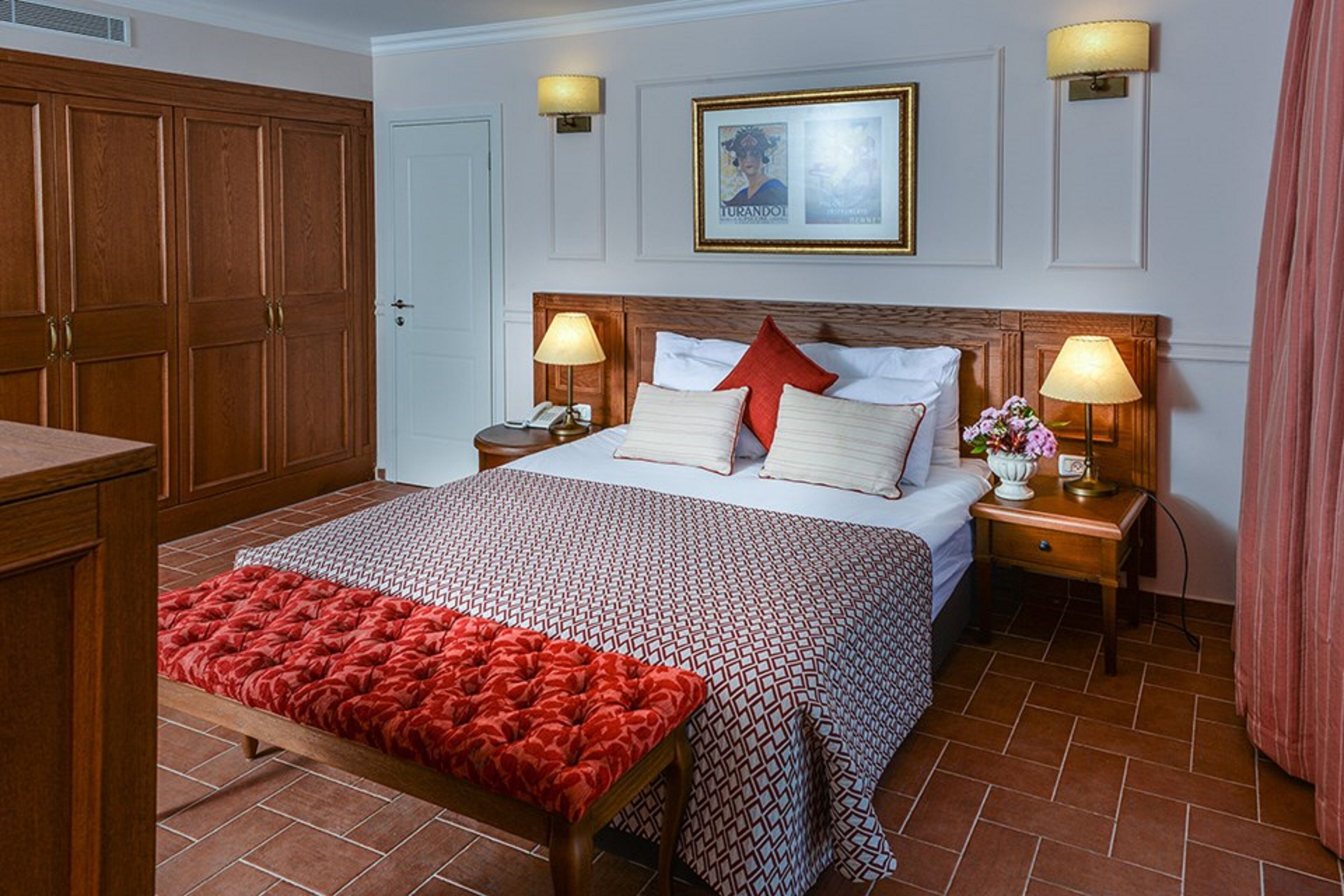 Habitació d'hotel amb un llit gran, dues taules de nit amb làmpades, un armari de fusta i un quadre encimbellat a la paret.
