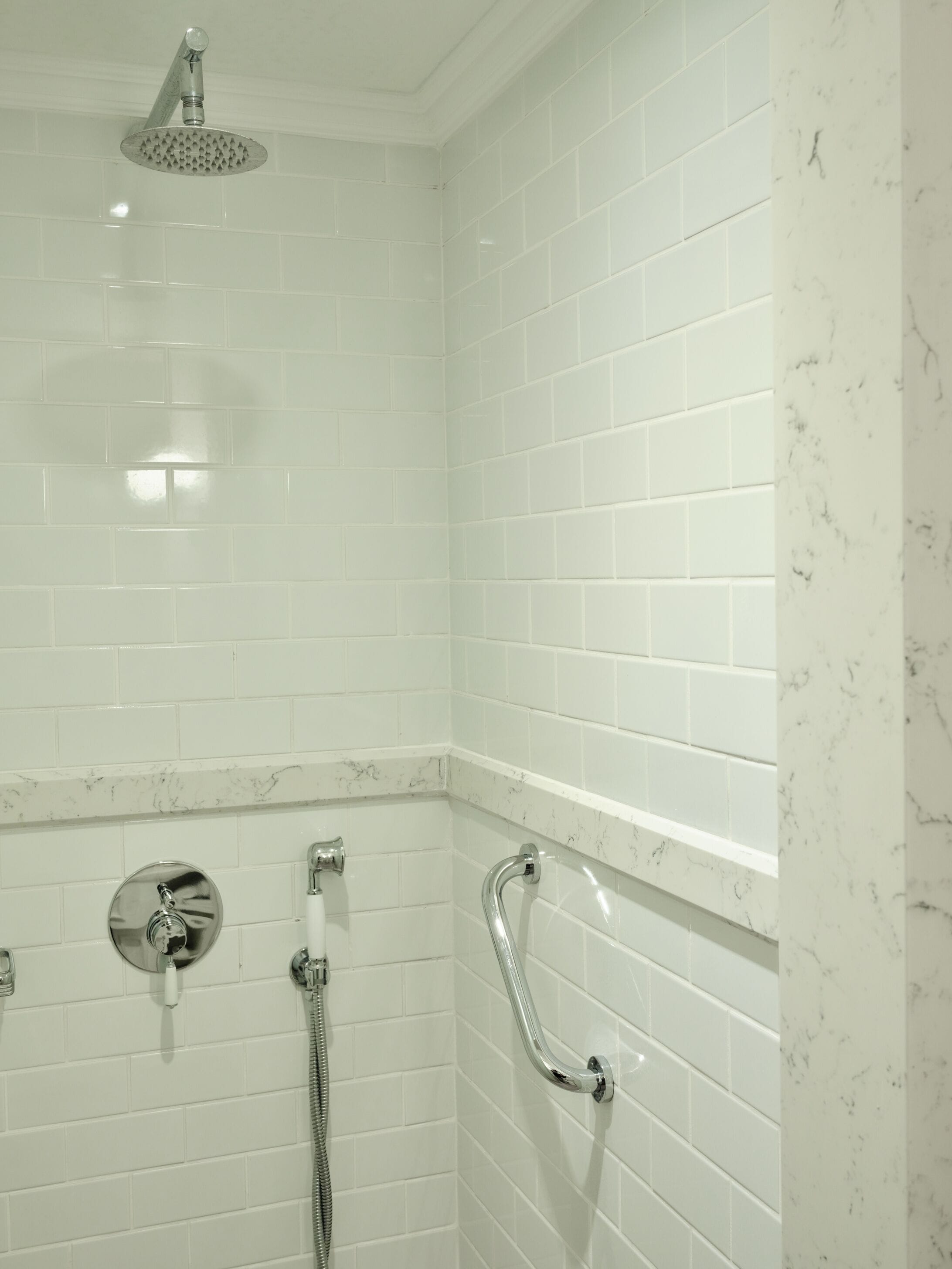 Un área de ducha con azulejos blancos y una pared de acento en mármol.