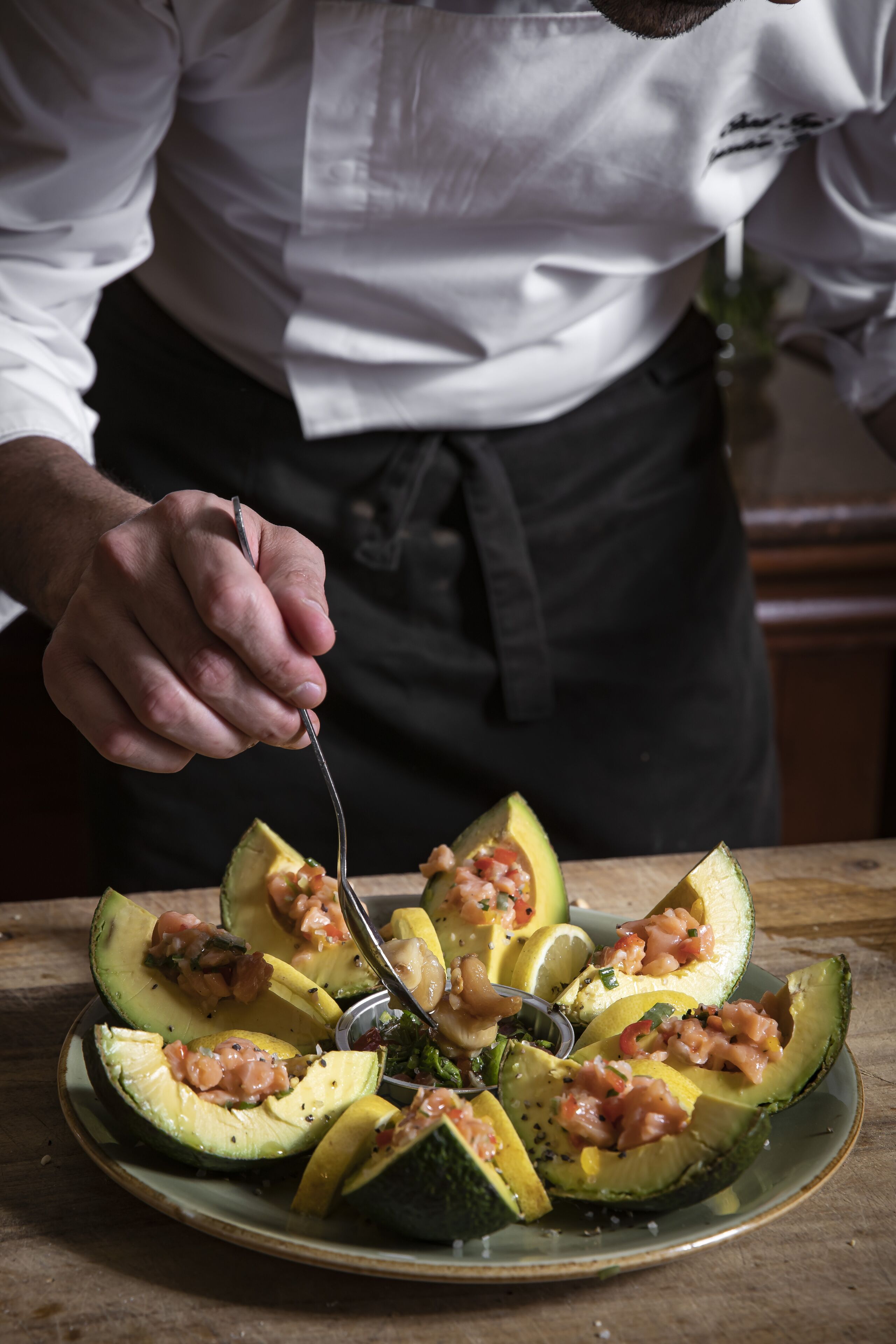 Een kok bereidt een gerecht met avocadohelften op een bord.