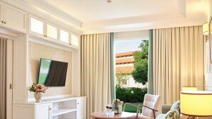 Een hotelkamer met een televisie op een witte kast, een eettafel met stoelen, een bank en een lamp.