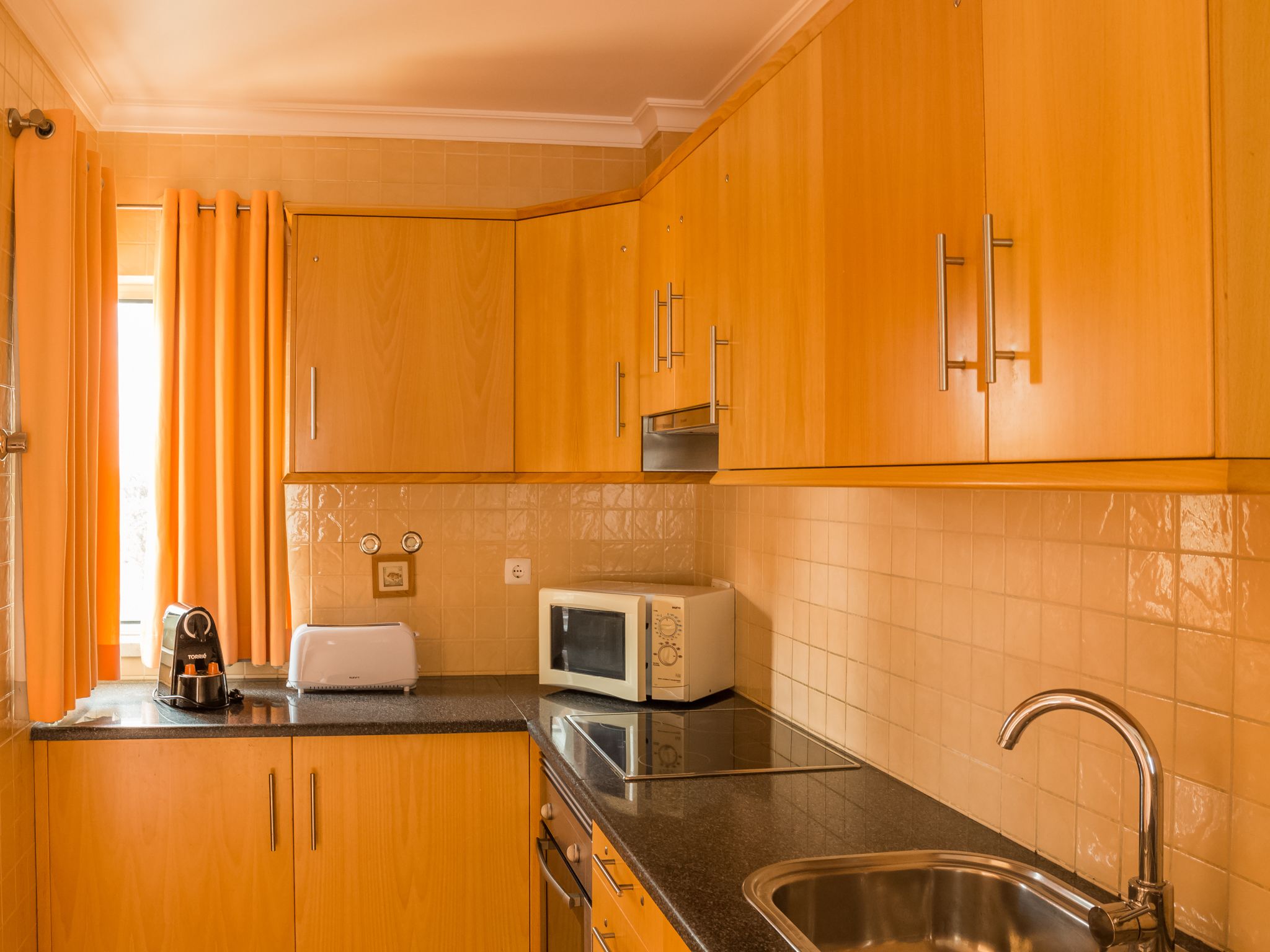 Una cocina con armarios de madera, microondas, tostadora y pileta.