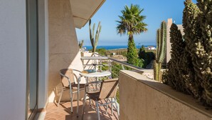 An outdoor patio with a table and chairs, overlooking a coastal landscape with cacti and a palm tree.
