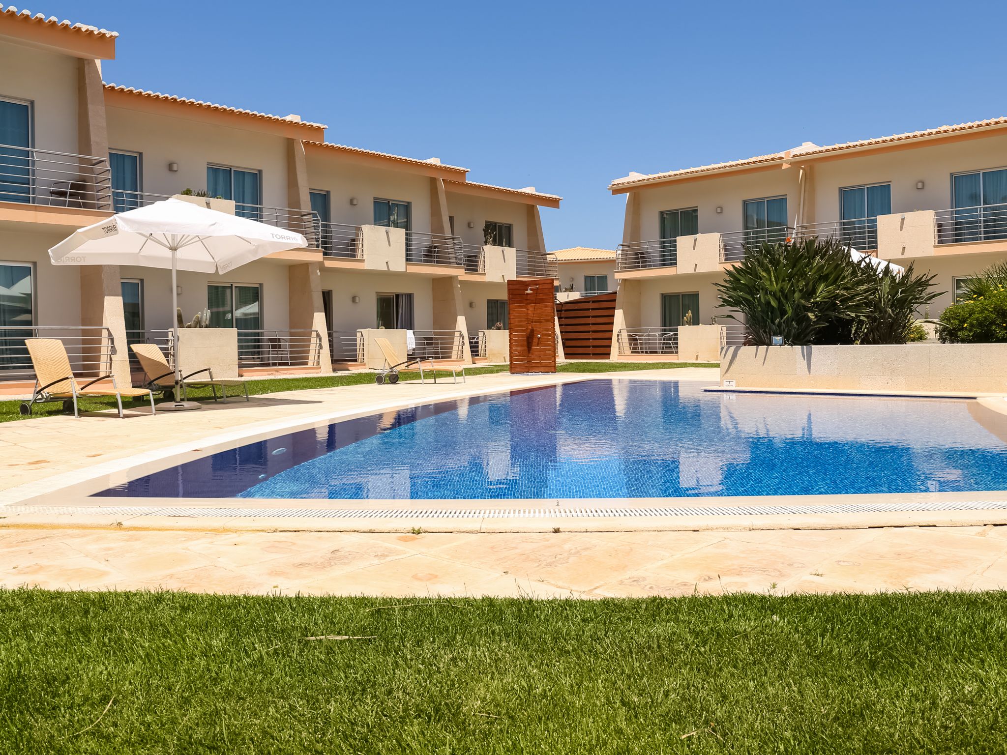 A swimming pool with lounge chairs and umbrellas, surrounded by a building with balconies and windows.