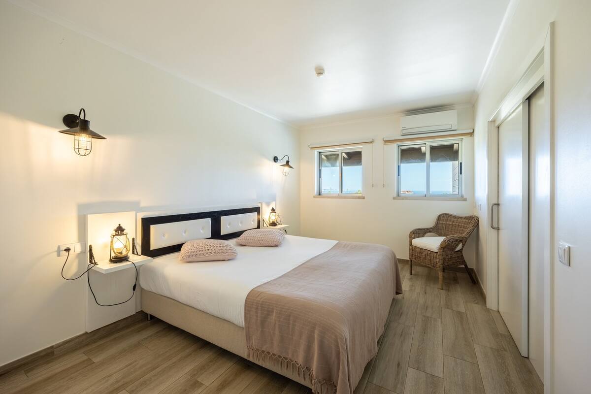 A bedroom with a bed, bedside lamps, a chair, and a window.