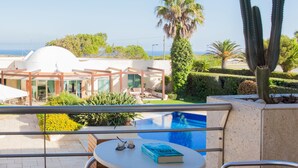 A balcony with a pool, a book, and sunglasses on a table.