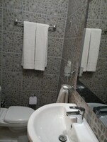 Un baño con un lavabo blanco, un inodoro y un espejo. Hay dos toallas blancas colgadas en toalleros. Las paredes presentan un diseño que imita a la piedra.