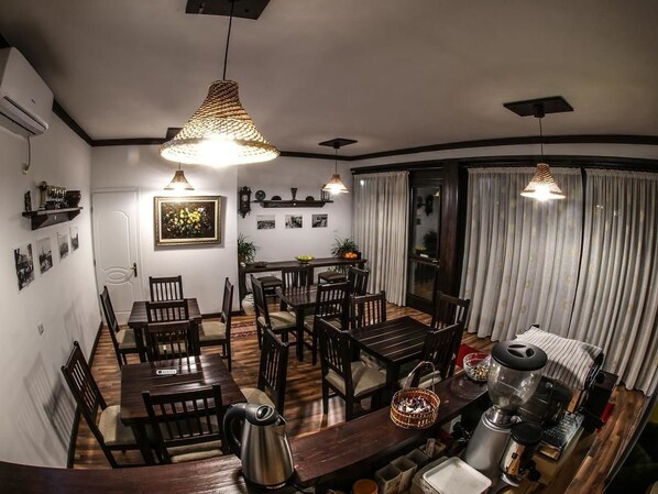 Un espace repas avec des tables et des chaises en bois, une machine à café et des lampes suspendues.