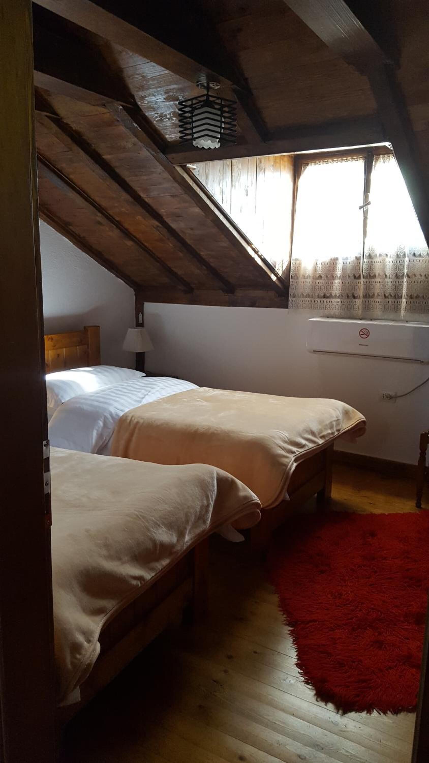 Una habitación con dos camas, un tapete rojo y una ventana con cortinas.