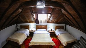 Habitación con tres camas alineadas, vigas de madera en el techo y una ventana que deja entrar luz natural.