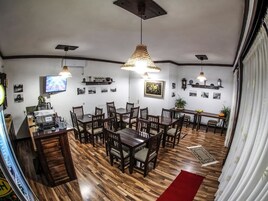 Comedor con suelo de madera, varias mesas y sillas, lámparas colgantes y adornos en la pared.