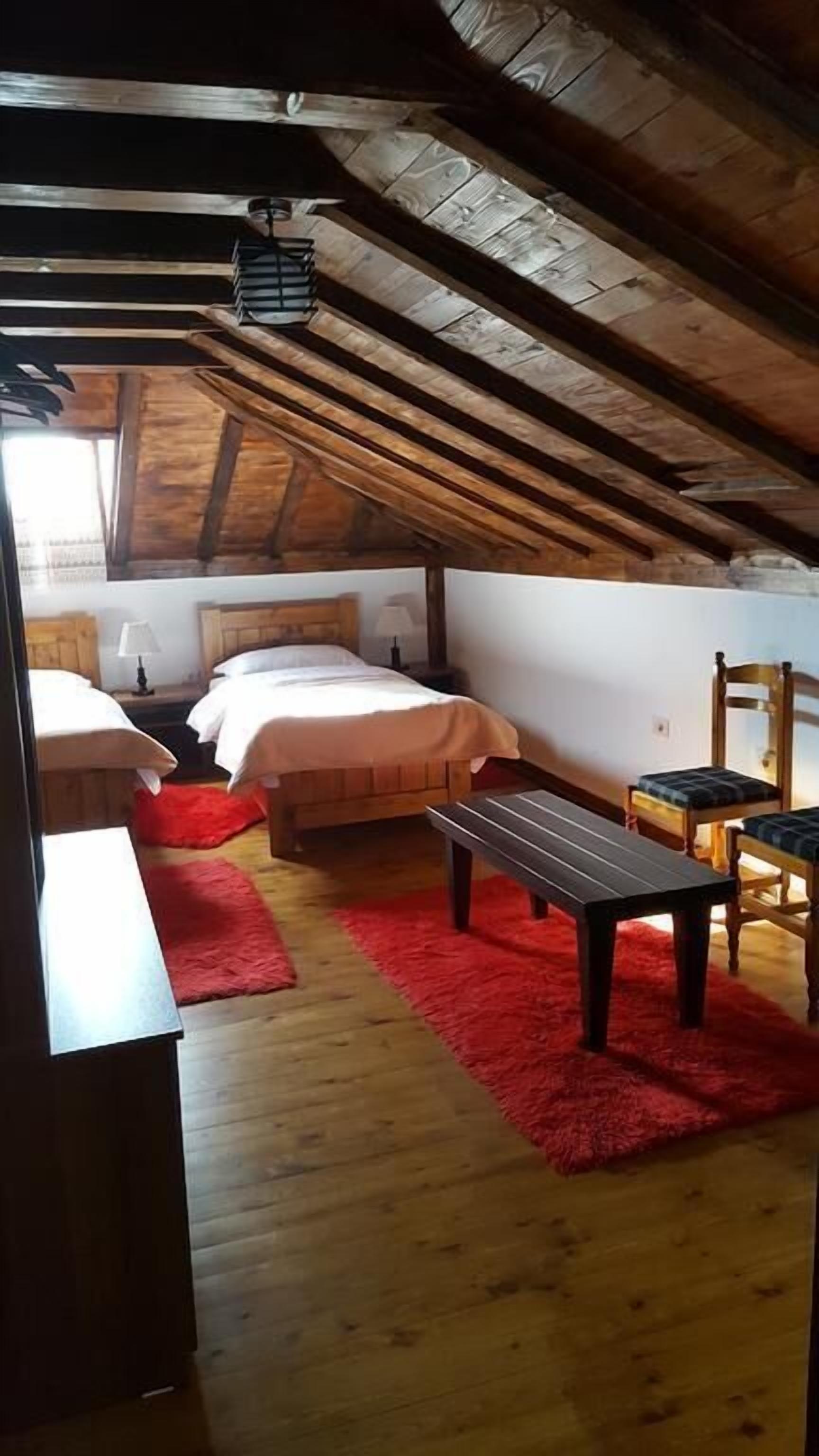 Une chambre confortable située dans les combles, avec des poutres en bois, un tapis rouge et deux lits.