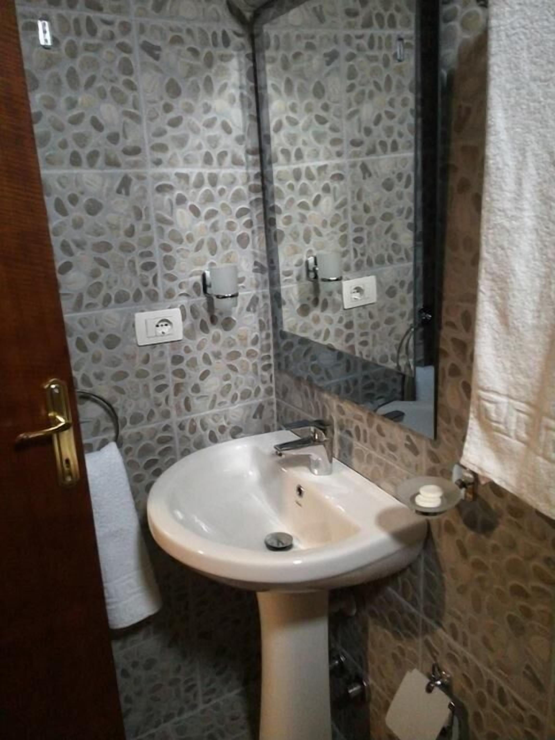 Ein Badezimmer mit einem weißen Waschbecken, einem Spiegel und einem Handtuch, das an der Tür hängt.