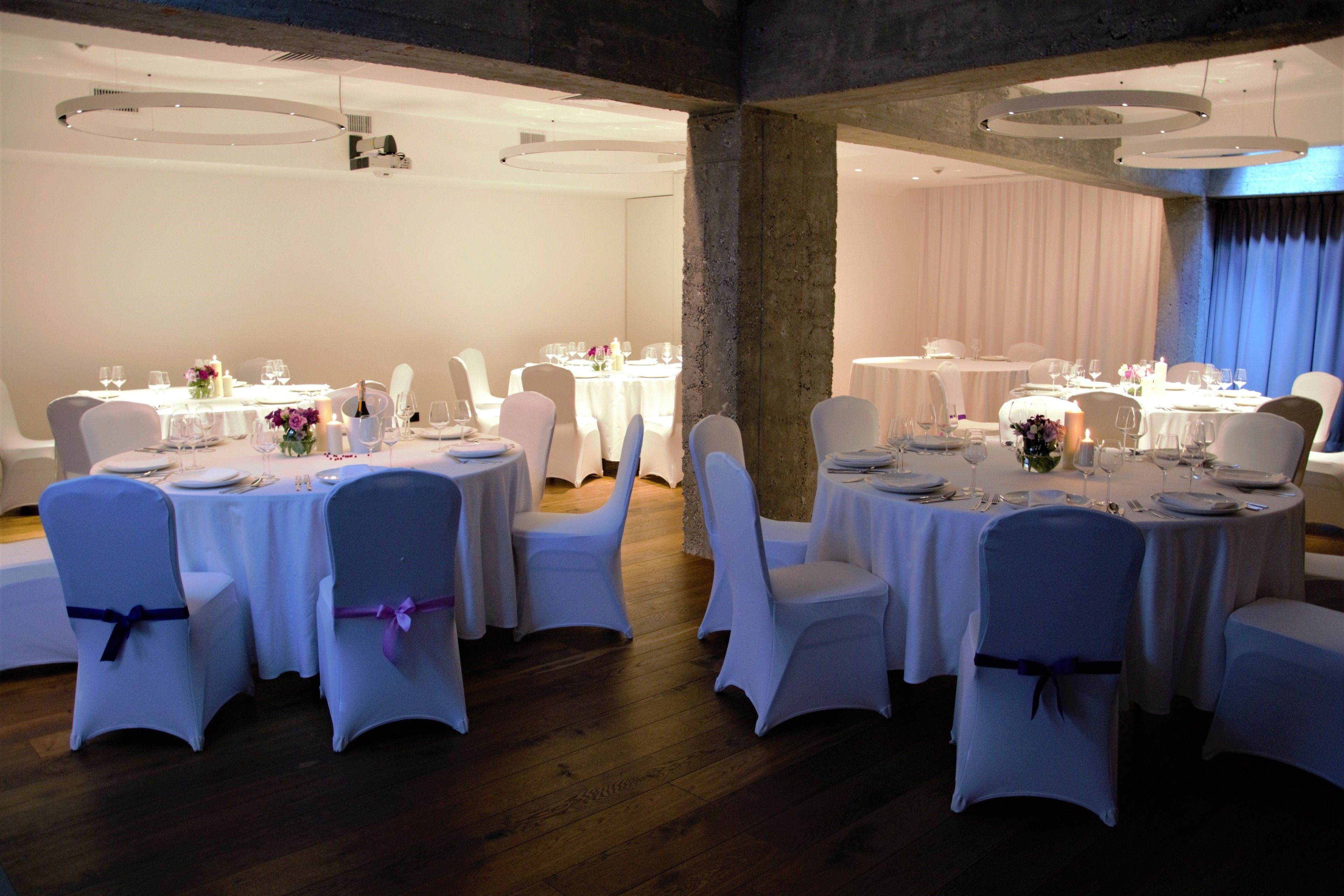 Un espai per a banquet amb taules rodones preparades per dinar, caires blancs i un terra de fusta.