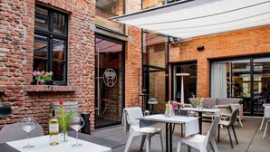 Un patio al aire libre con mesas y sillas, un muro de ladrillo y un acceso por una puerta de vidrio.