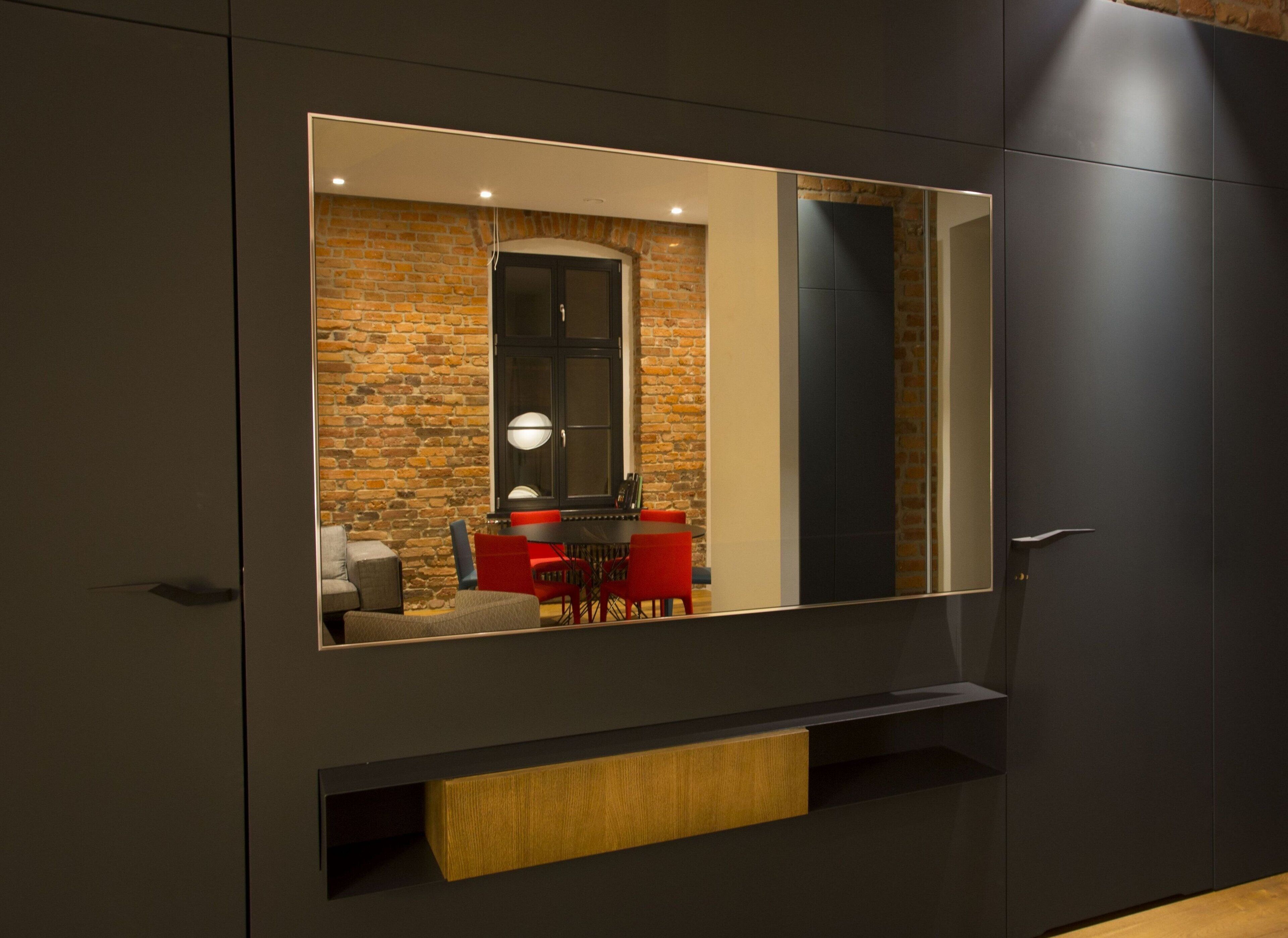Une pièce moderne dotée d’un grand miroir qui reflète un coin repas avec des chaises rouges et un mur en briques.