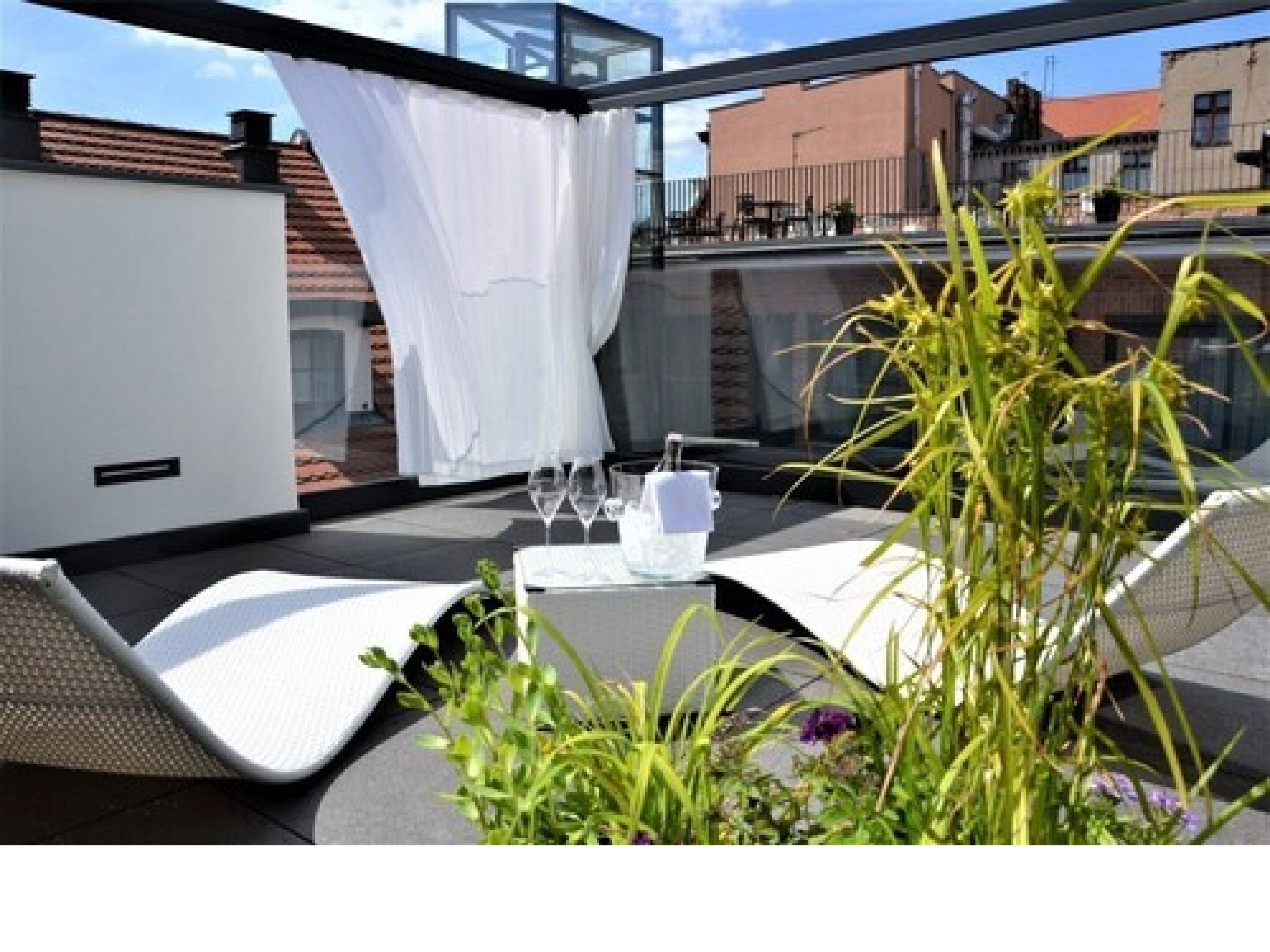 Una terraza en la azotea con mobiliario exterior, una mesa dispuesta para dos personas y vistas a la ciudad.