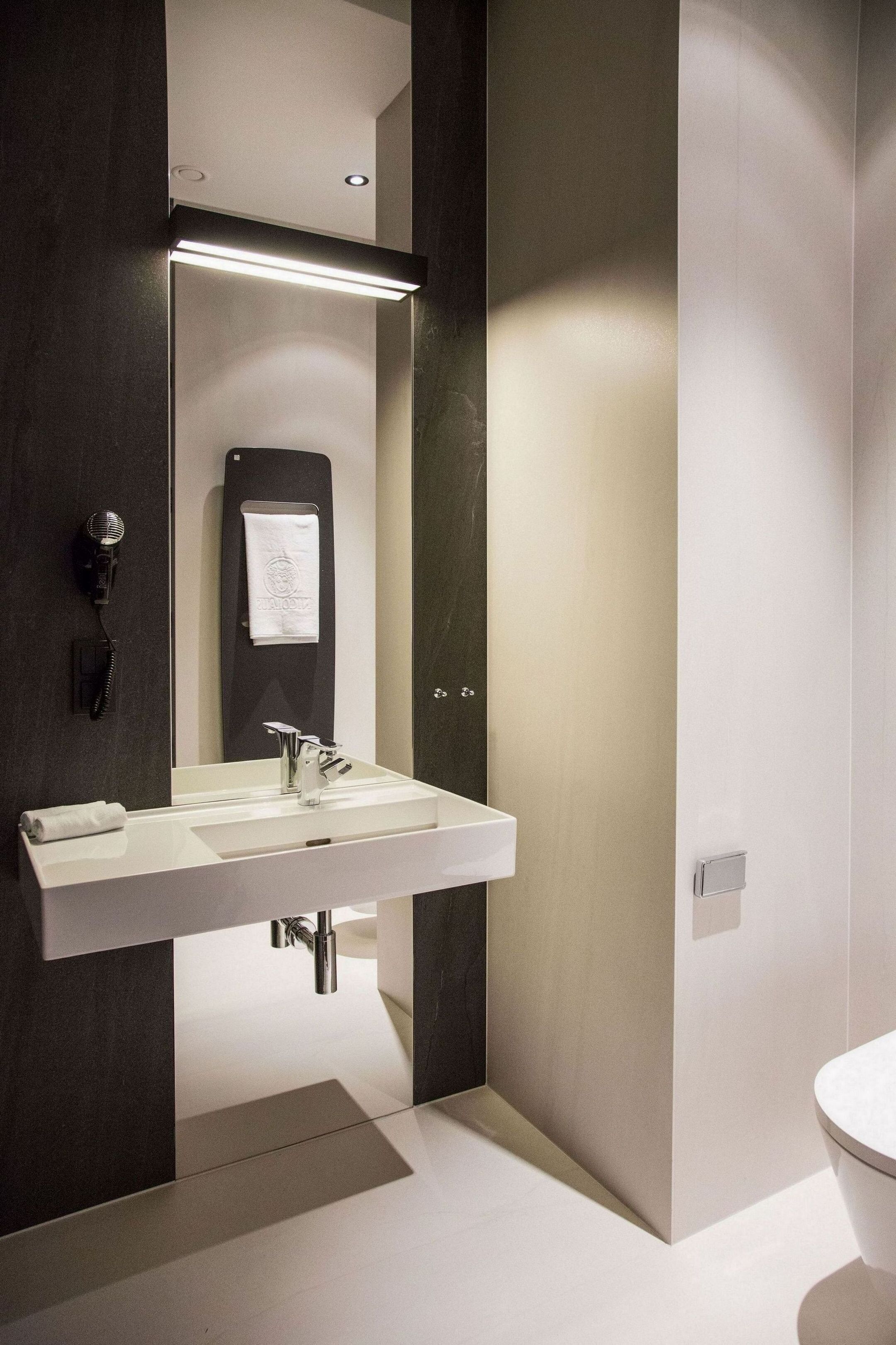 Un baño moderno con un espejo grande, un secador de pelo y una toalla colgada en la pared.