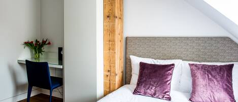 A bedroom with a sloped ceiling, a wooden accent wall, a desk with a chair, and a bed with two pillows.