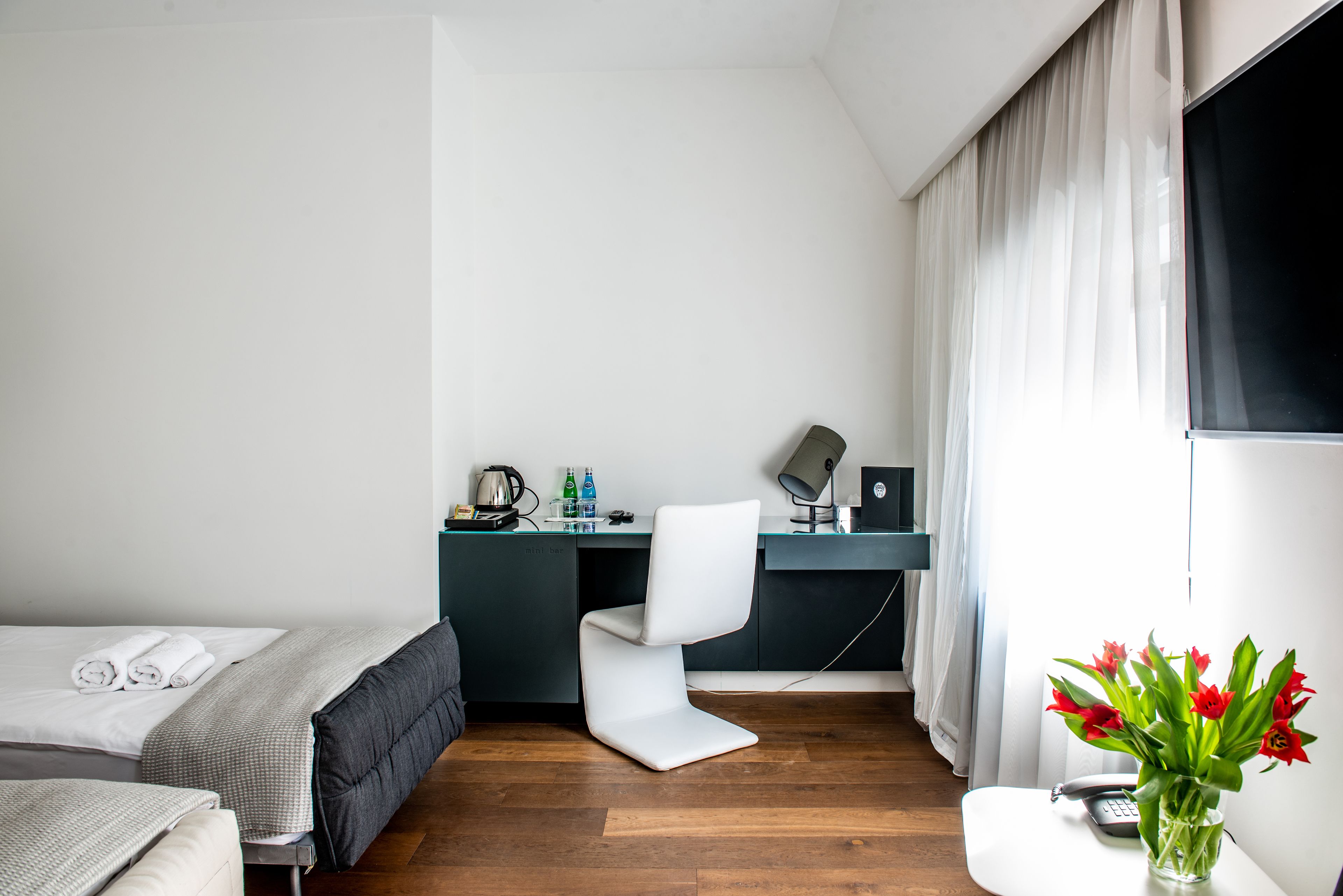 Una habitación de hotel moderna con una cama, un escritorio, una silla, una mesita y un jarrón con flores.
