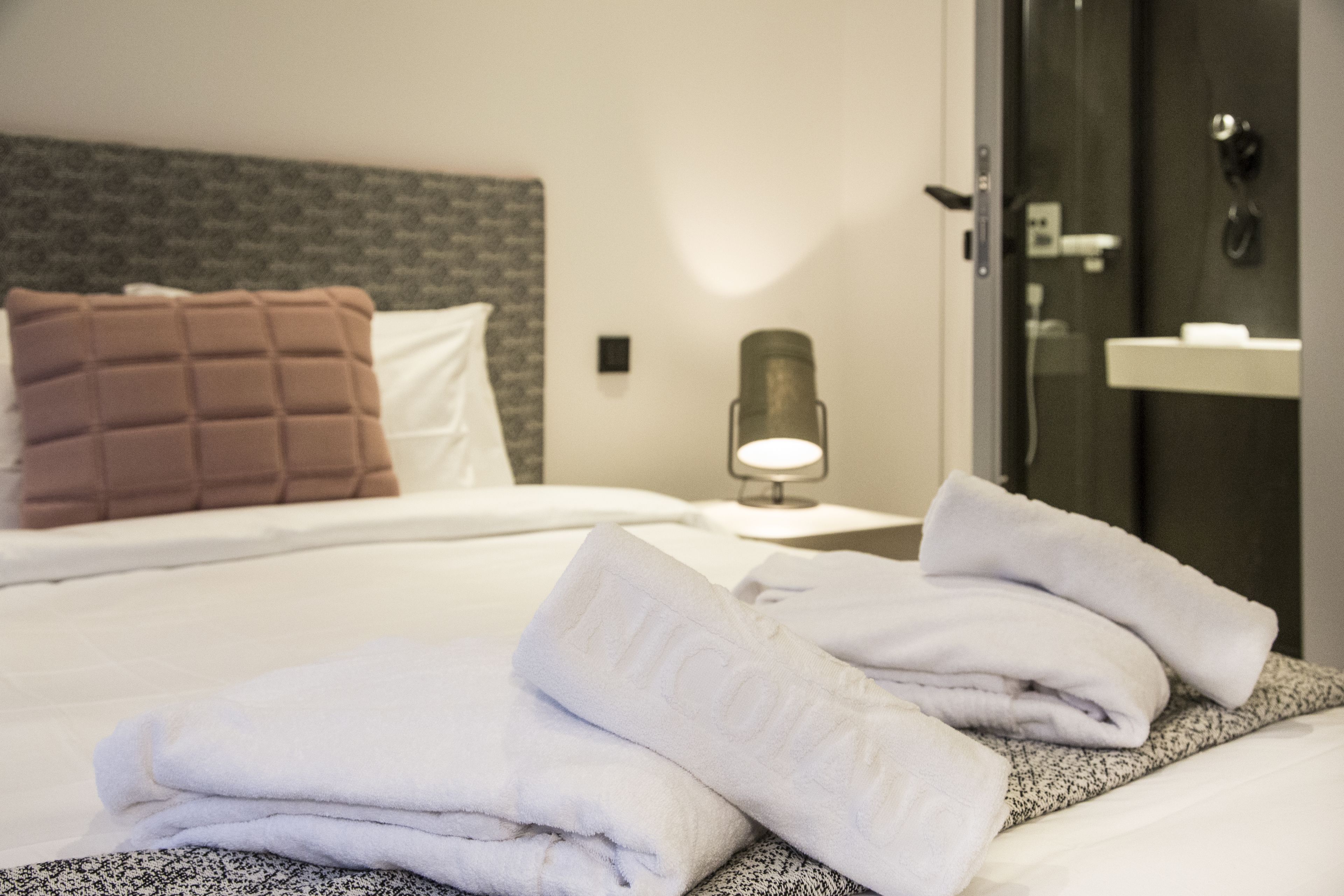 A neatly made bed with folded white towels and a brown pillow.