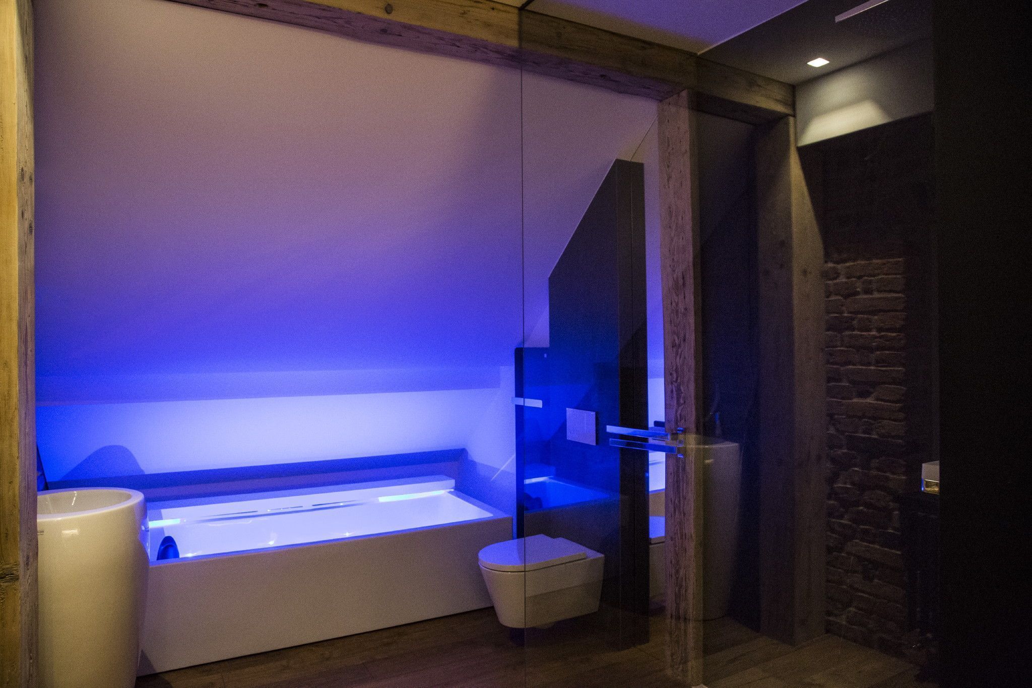 A modern bathroom with a glass-enclosed bathtub, a white toilet, and a wooden floor.