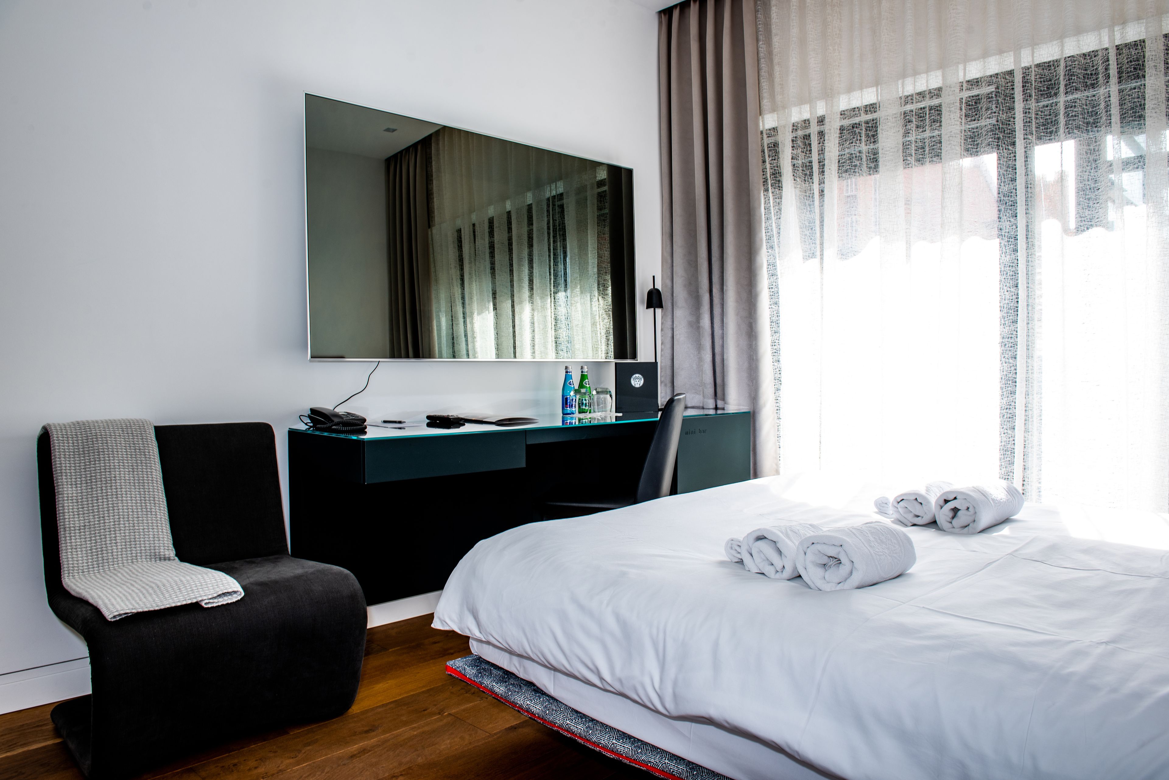 A hotel room with a bed, a desk, a chair, a large mirror, and a window with curtains.