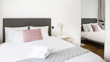 A modern hotel room with a large bed, a bedside table with a vase of flowers, and a mirror on the wall.