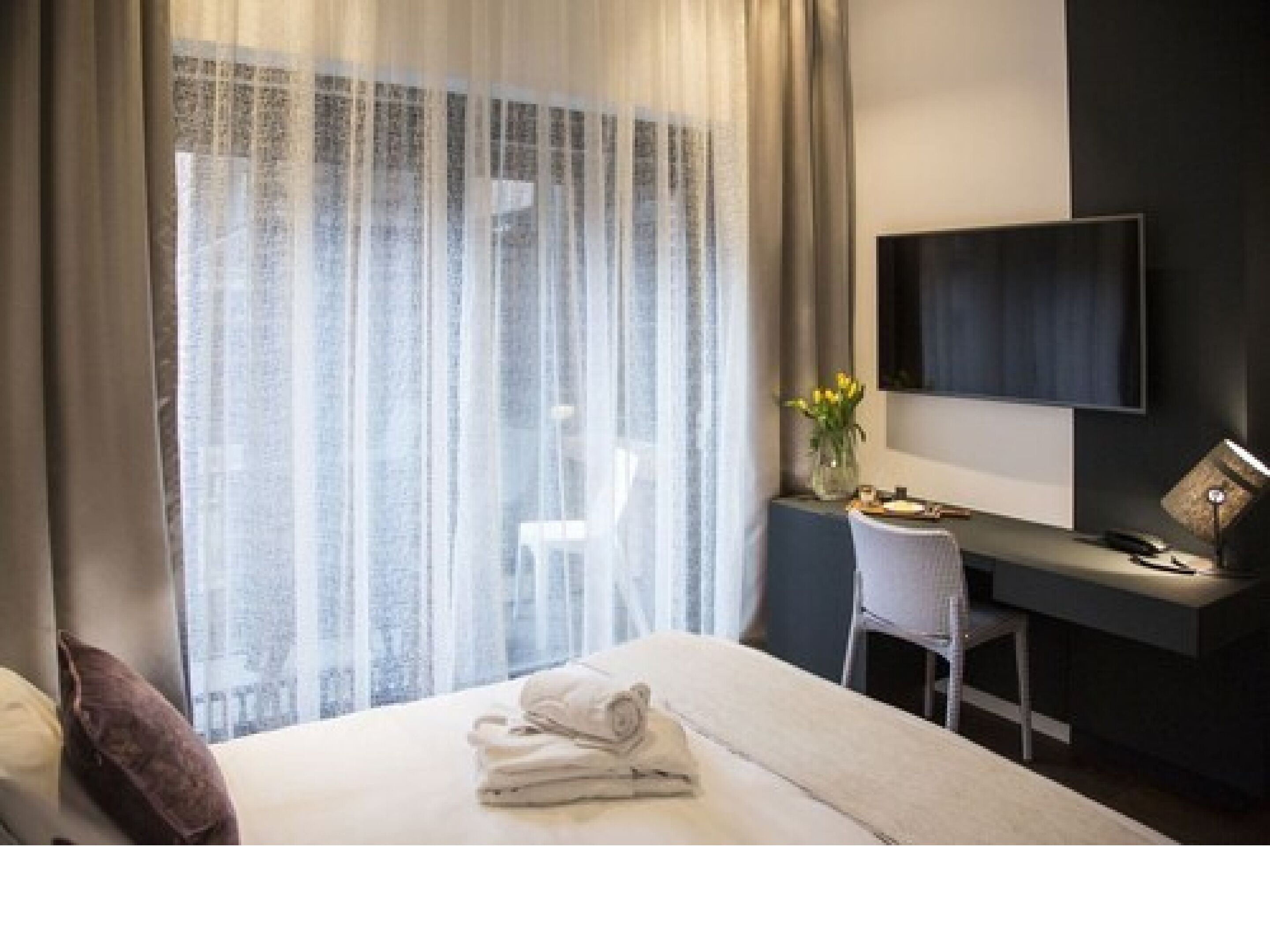 Ein Hotelzimmer mit einem Bett, einem Schreibtisch, einem Sessel, einem Flachbildfernseher und einem Fenster mit durchsichtigen Vorhängen.