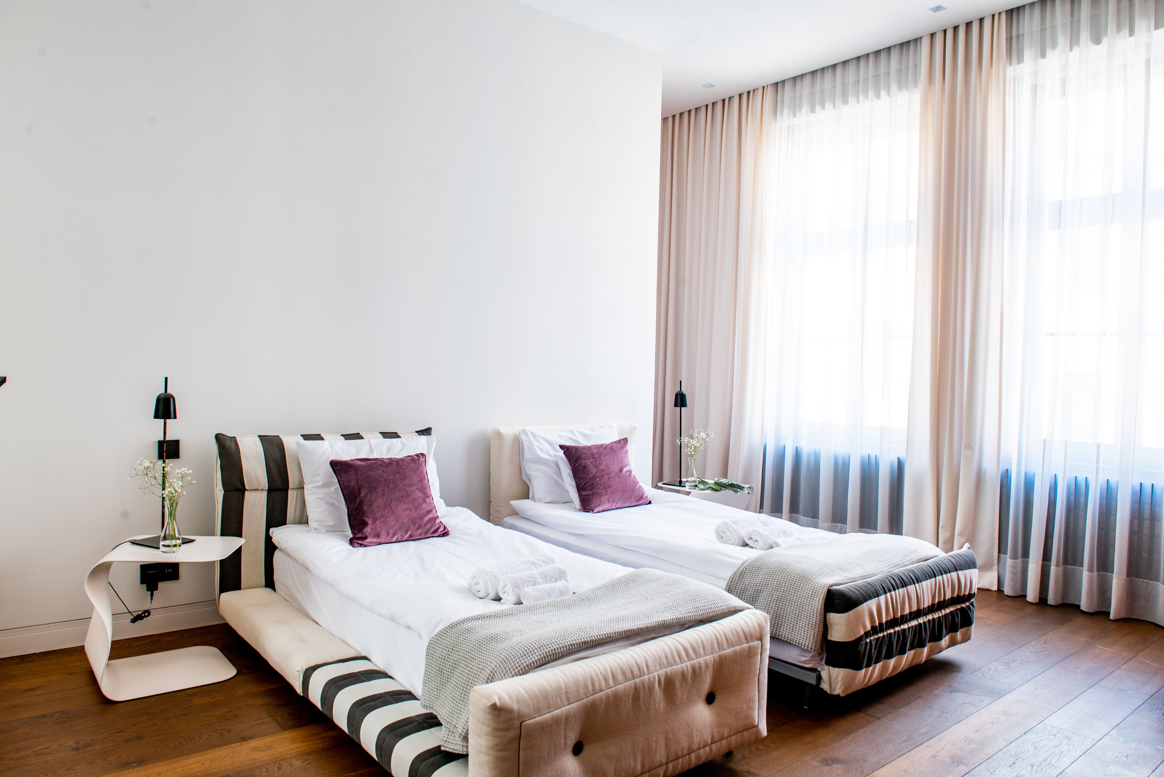 A hotel room with two beds, a bedside table, a lamp, and a window with curtains.