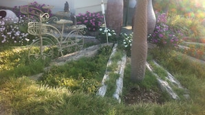 Un jardín con una escultura de metal, jarrones grandes y plantas en flor.