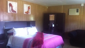 Una habitación de hotel con cama, mesita de noche, una silla y una puerta que da a otra estancia.